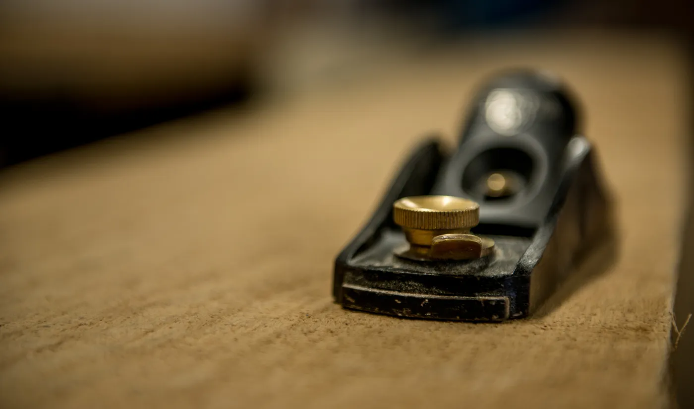 Close-up of a vintage hand plane with a brass adjustment knob on a workbench, reflecting traditional craftsmanship